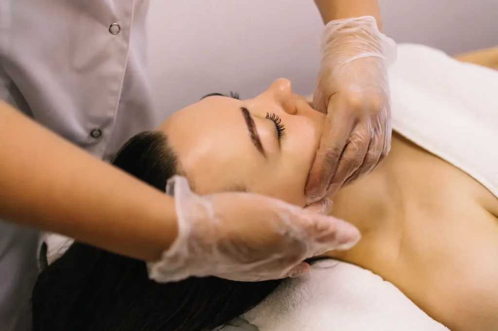 Practitioner uses both hands along a reclining woman's jaw and cheek during a facial massage.