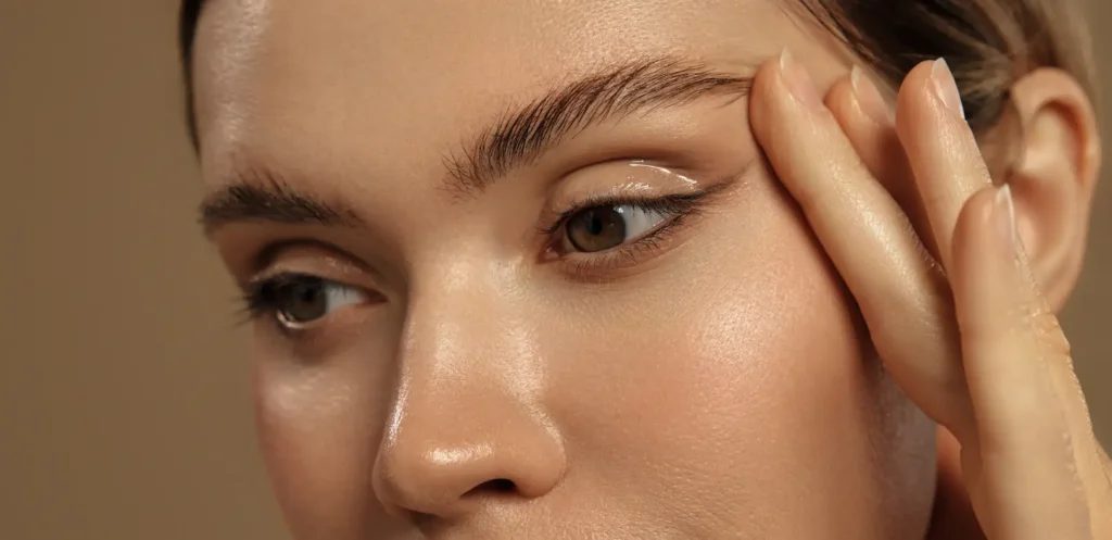 Close-up of a woman's eyes and eyebrows as her fingers rest beside the outer corner of one eye.